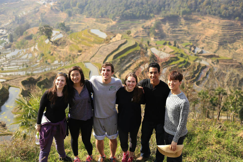 Students stand on a hillside overlooking a valley with terraced fields.