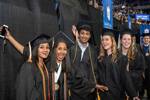 A group of students in graduation caps and gowns pose and smile at the camera