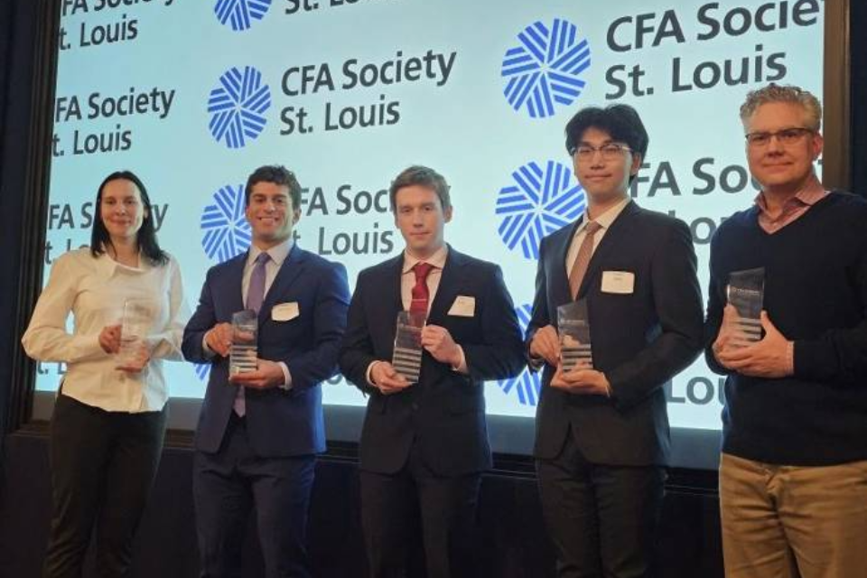 Four students and a professor stand in a row, holding awards, in front of a screen that reads CFA Society Saint Louis