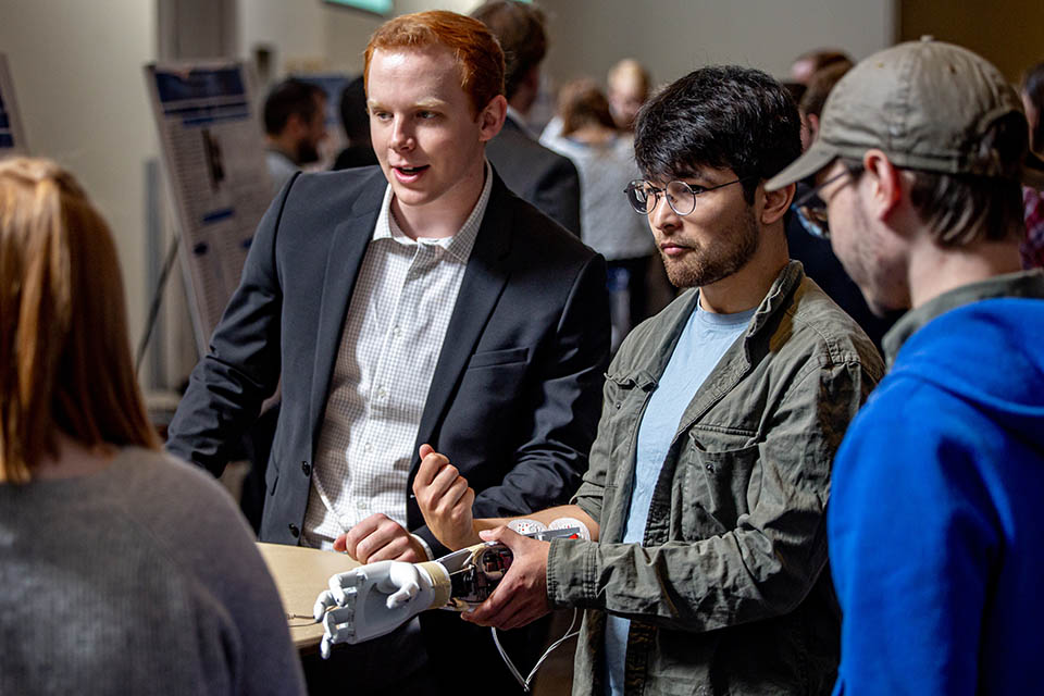 Shakhboz Hasanov, center, and Matthew Draper, left, demonstrate their team’s project “Myoelectric Prosthesis for Below Elbow Amputation” during the Senior Legacy Symposium on May 2, 2023. Photo by Sarah Conroy. 