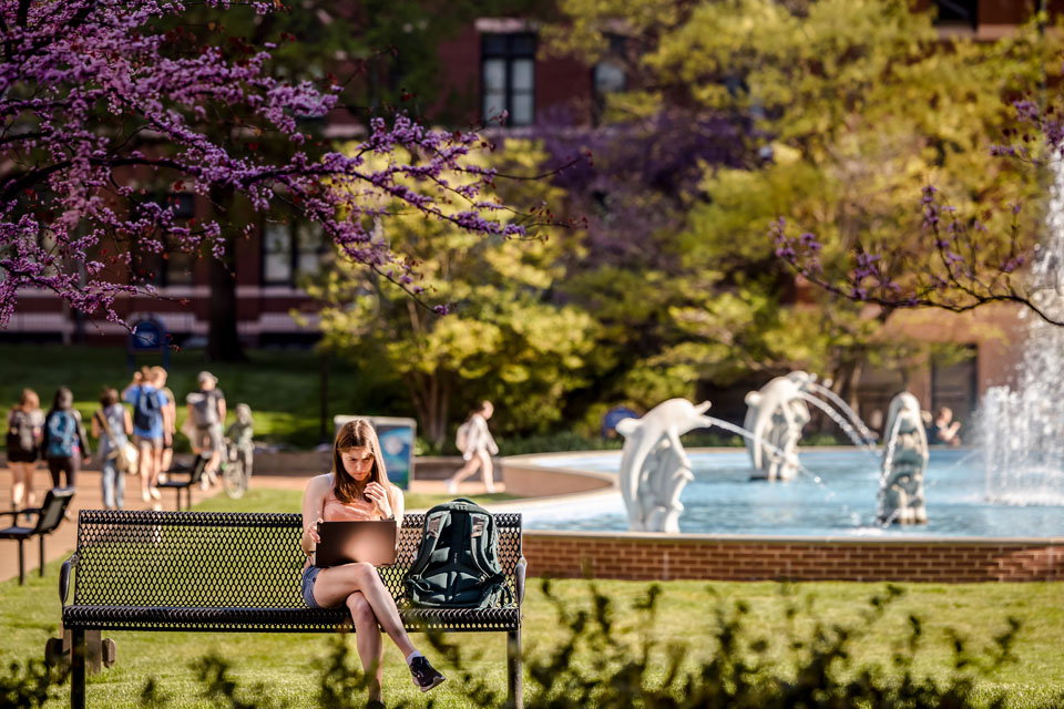 A student sits on a bench by the Dolphin Pond on April 14, 2023. Photo by Sarah Conroy.
