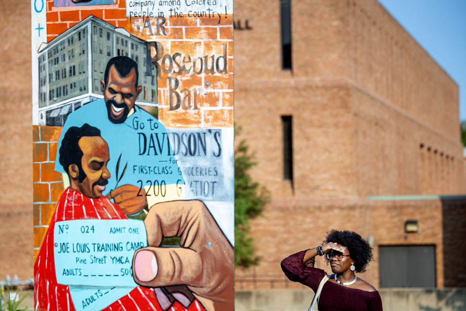 A person reads the back of a piece from “The Legacy of Mill Creek,” an art installation by Cbabi Bayoc surrounding the fountain at Grand and Lindell Blvds. The installation honors the vibrant historically Black community that lived in the former Mill Creek Valley neighborhood