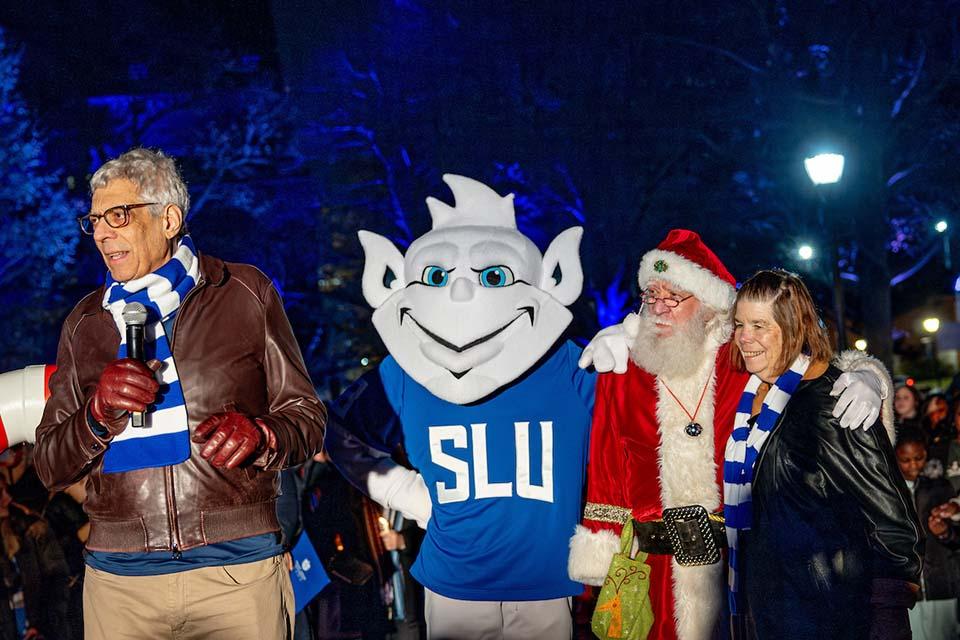 The Billiken, Santa Claus, University President Fred Pestello, Ph.D., and Fran Pestello, Ph.D., stand together at Christmas on the Quad. Photo by Sarah Conroy.