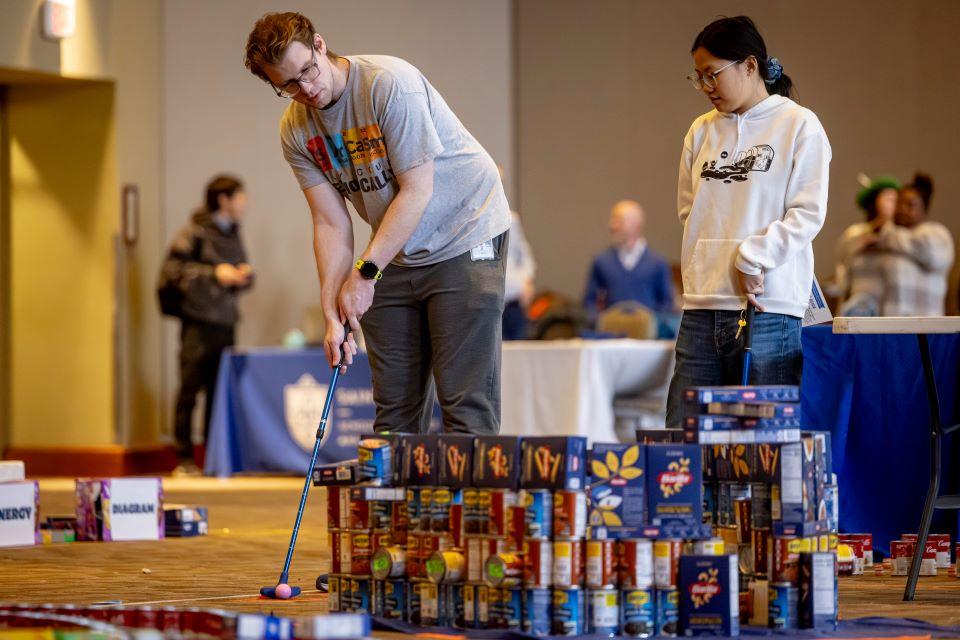 Members of the SLU community play miniature golf on a course constructed from shelf-stable grocery items at Golf and Give, an SSE Innovation Challenge to benefit Billiken Bounty on February 25, 2025. Photo by Sarah Conroy.