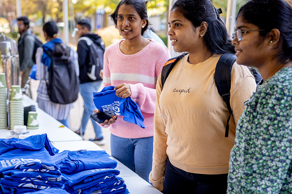 Three students talk and select T-shirts from a table.