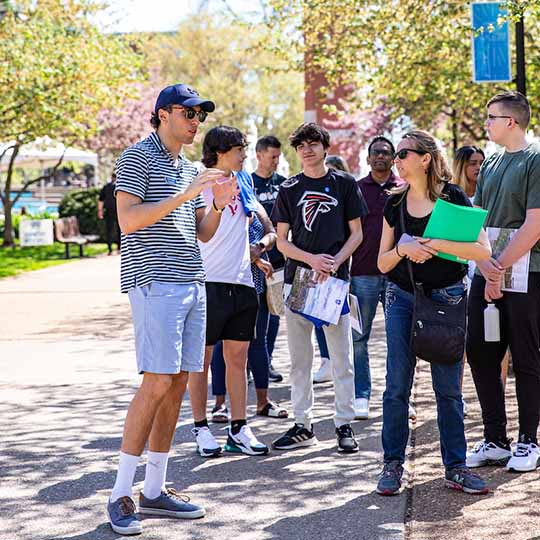 Group of students standing with a tour leader near the clock tower during a campus visit