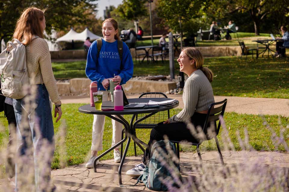 Three students enjoying a conversation outside next to a table