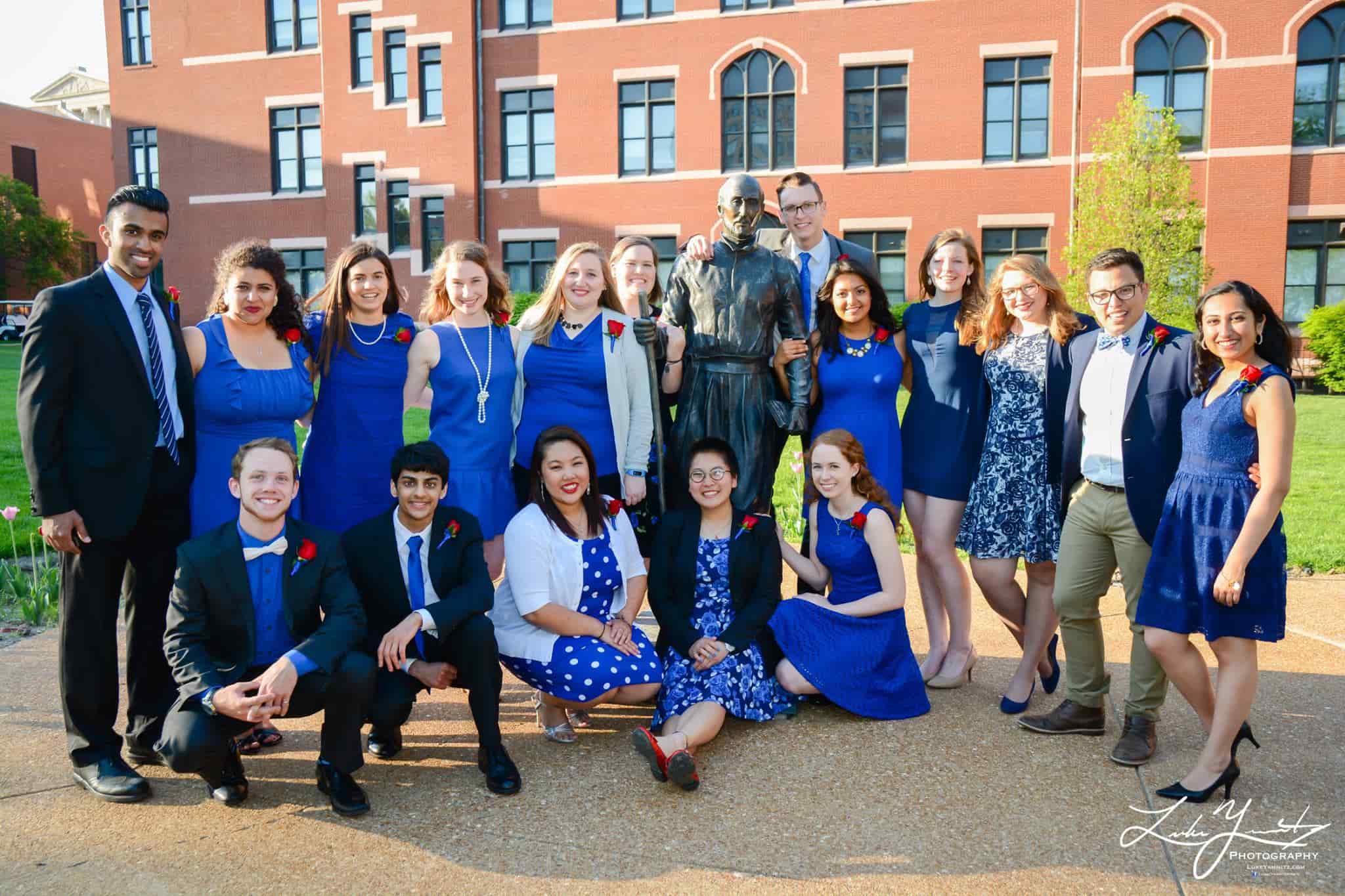 A group of students pose for a photo outside with a campus building in the background.