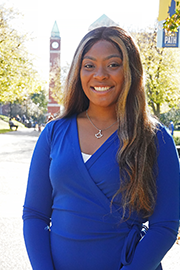 A headshot photo of Kelci Crandall with a clocktower and trees in the background.