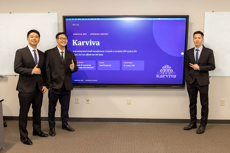 Karviva Project Three students pose for a photo next to a screen at the front of a classroom.