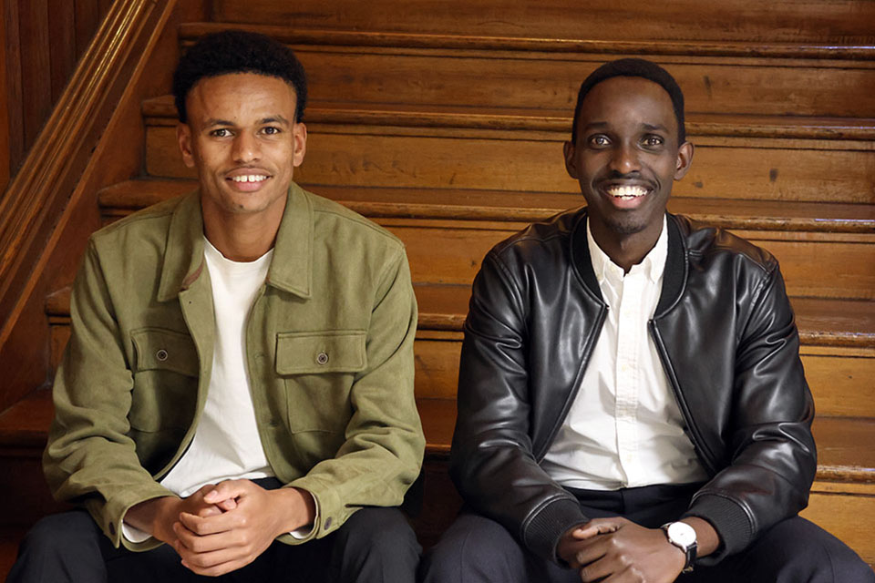 Two men pose for a photo together sitting on wood steps.