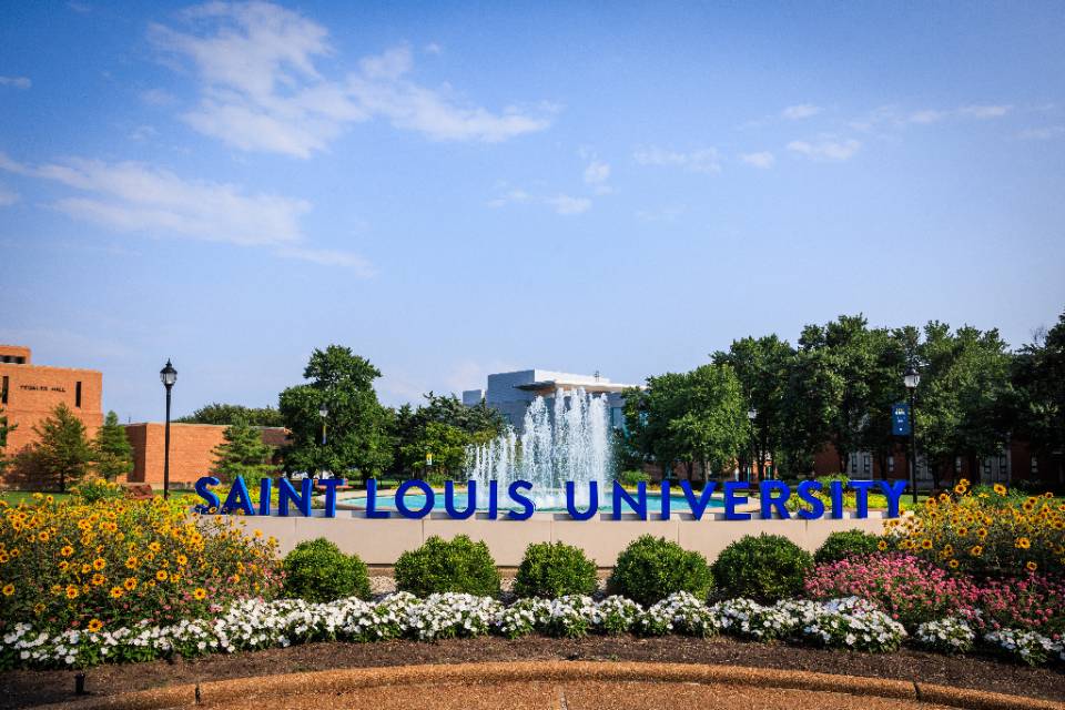 Scene of SLU fountain with flowers with Saint Louis University spelled out in large letters and displayed on the edge of the fountain