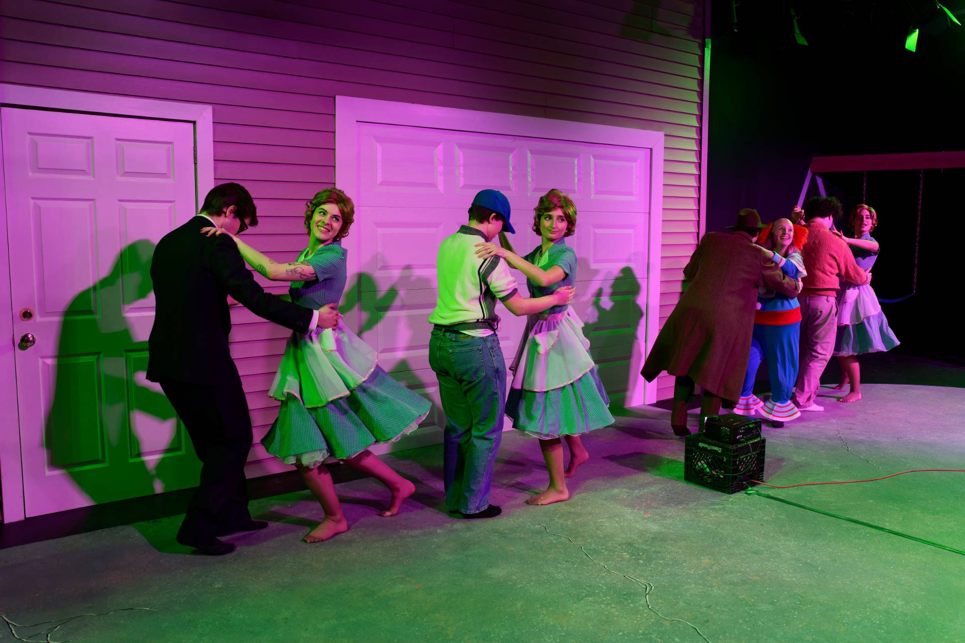 A group of people dance in pairs under purple and green background