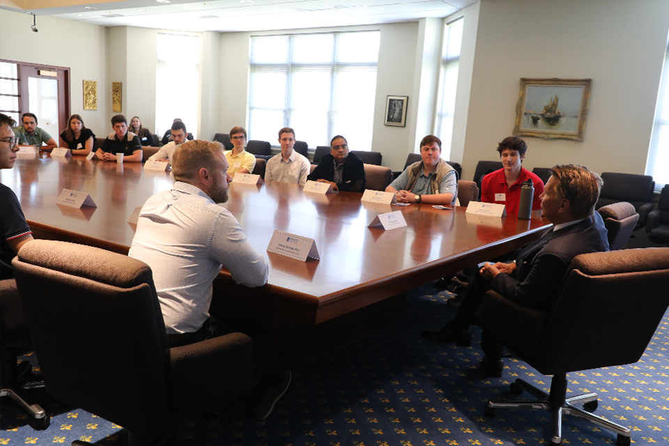 Stifel CEO Ron Kruszewski sits at the head of a boardroom table and offers his advice to group of finance students seated around the table.