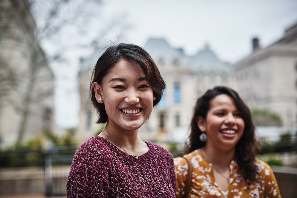 Two SLU students smiling outside in the courtyard of the Chaifetz School of Business on a sunny day. 