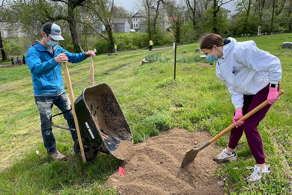Two SLU students shovel dirt outdoors as part of a Service Day activity. 