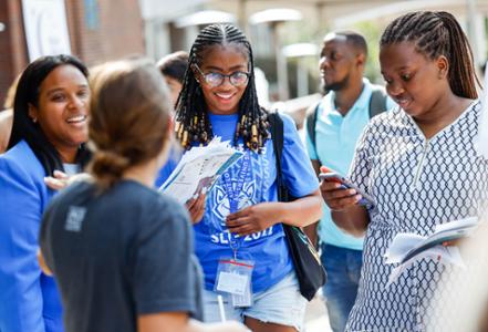 Three students talk to another while visiting a table at the D I C E Resource fair.