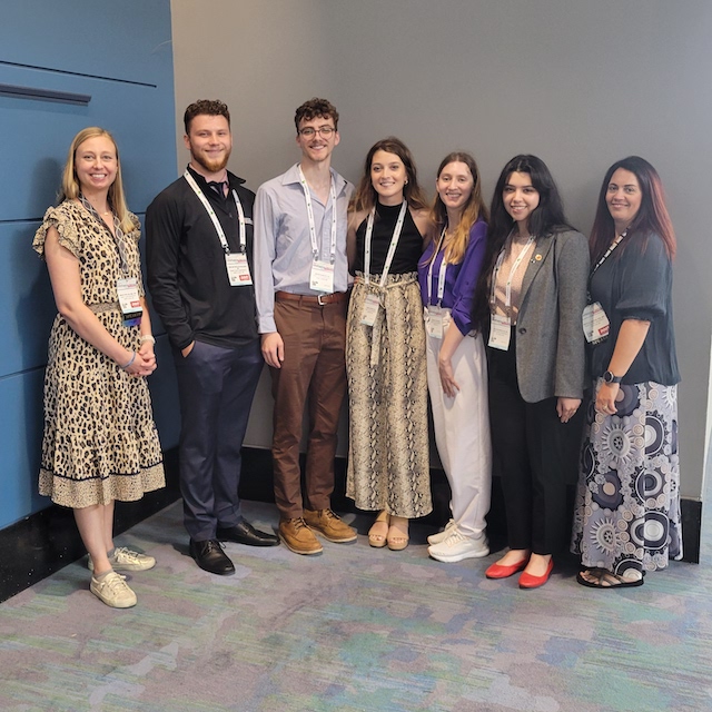 NMT students and faculty standing together in front of a blue and gray wall