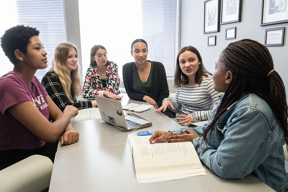 Six students sit around a table, talking