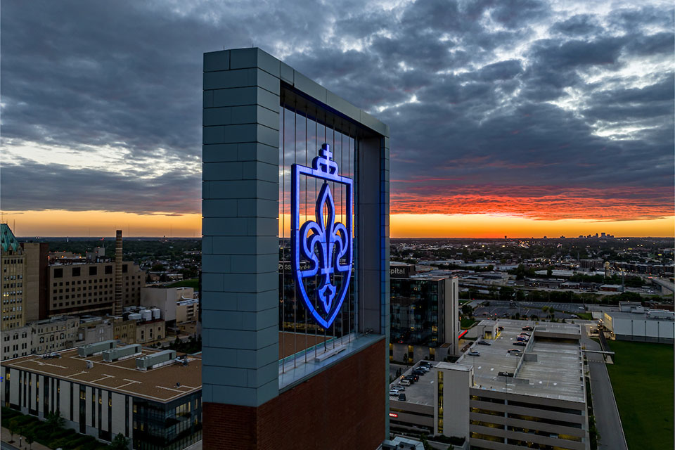 A SLU logo lights up on top of a building at sunset.