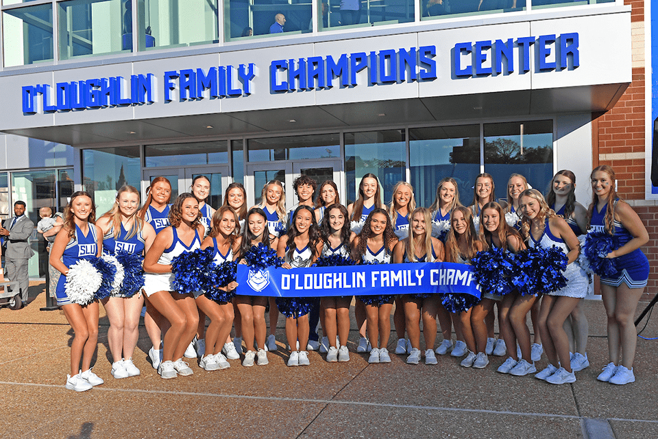 A group of cheerleaders pose for a photo with a banner that states o'loughlin family champions center