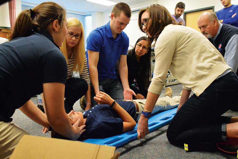 A student lies on a back board surrounded by other students and instructors during a demonstration.