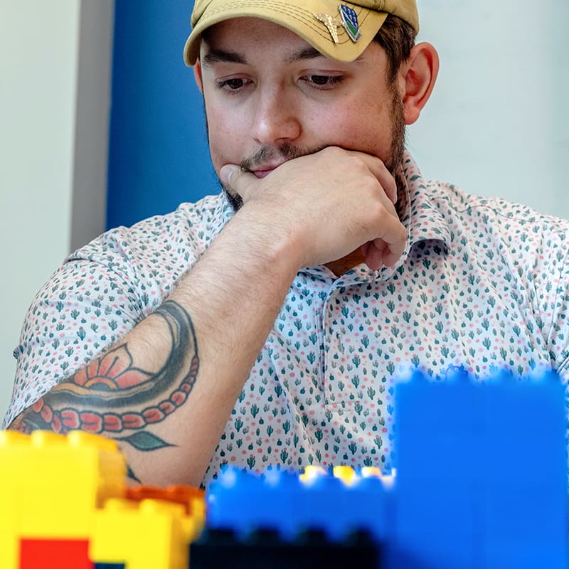 A student rests his chin on his hand while examining legos during a community-planning class.