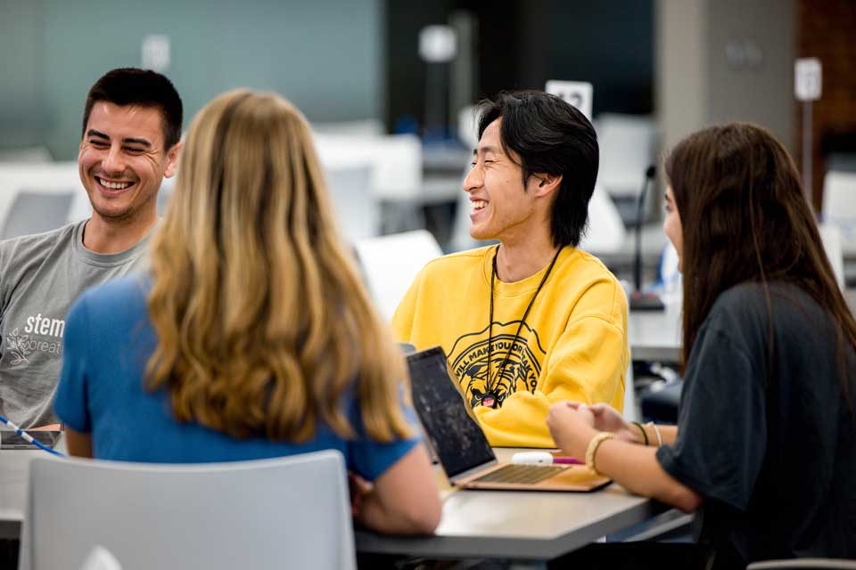 Students around a table interact in a college classroom