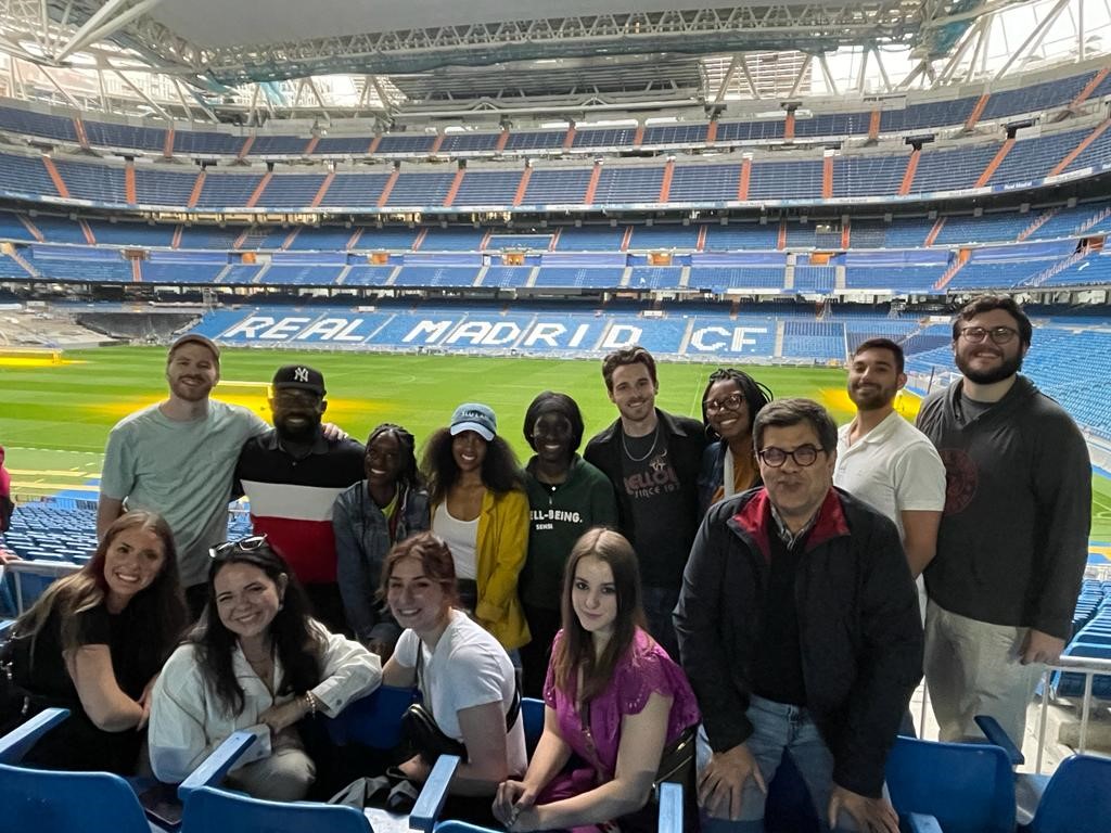 Students pose in seats at a stadium, with the field in the background.