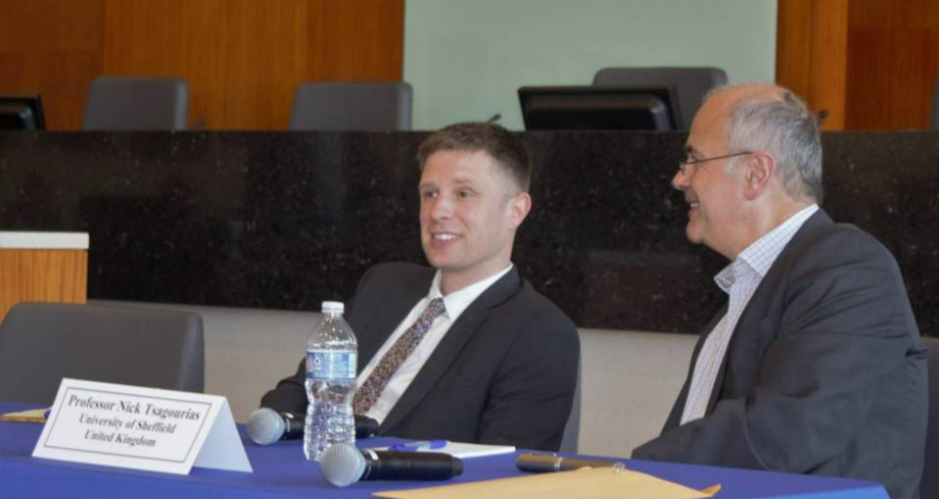 Two panelists talk while sitting at a table.