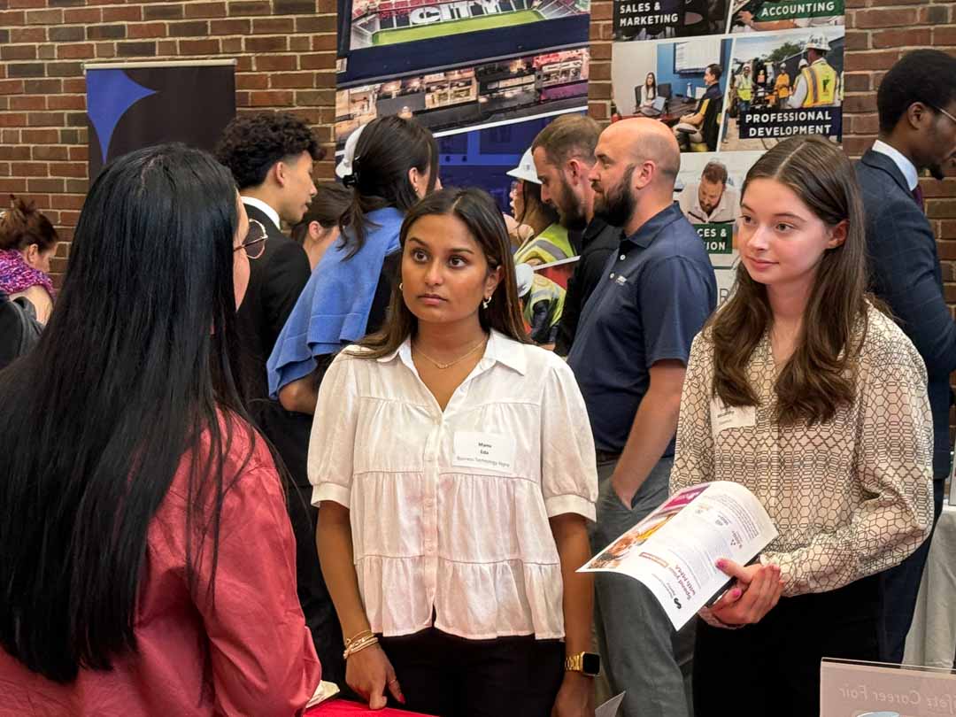 Two students talk to an employer in a room filled with people.