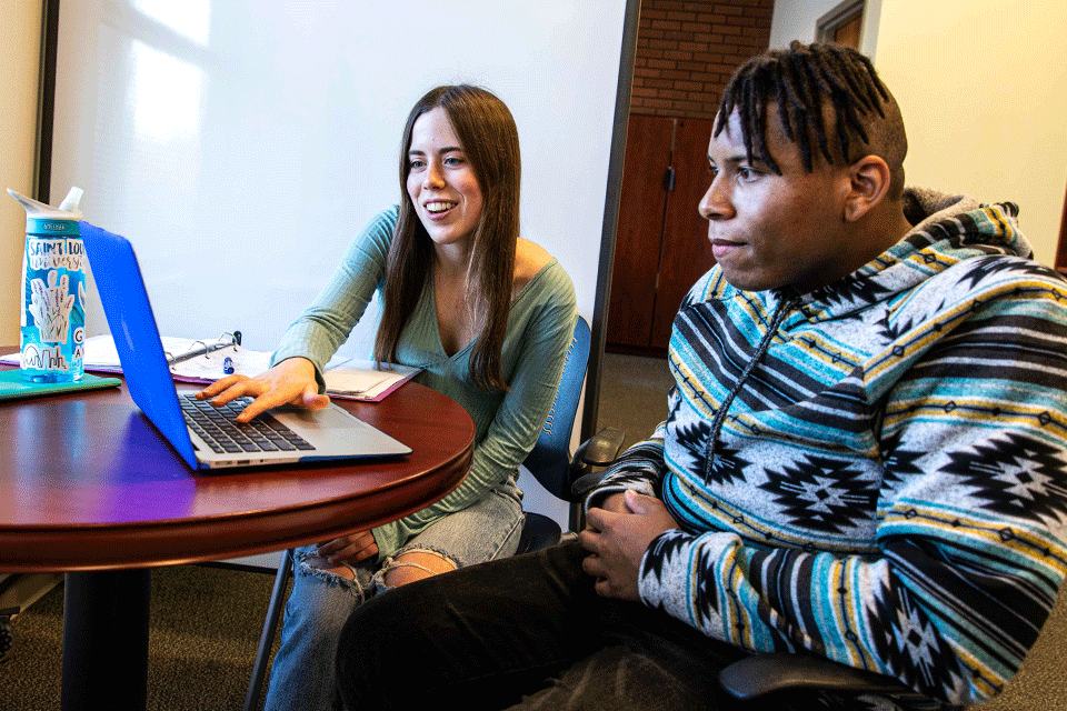 Two students sitting at a table looking at a computer