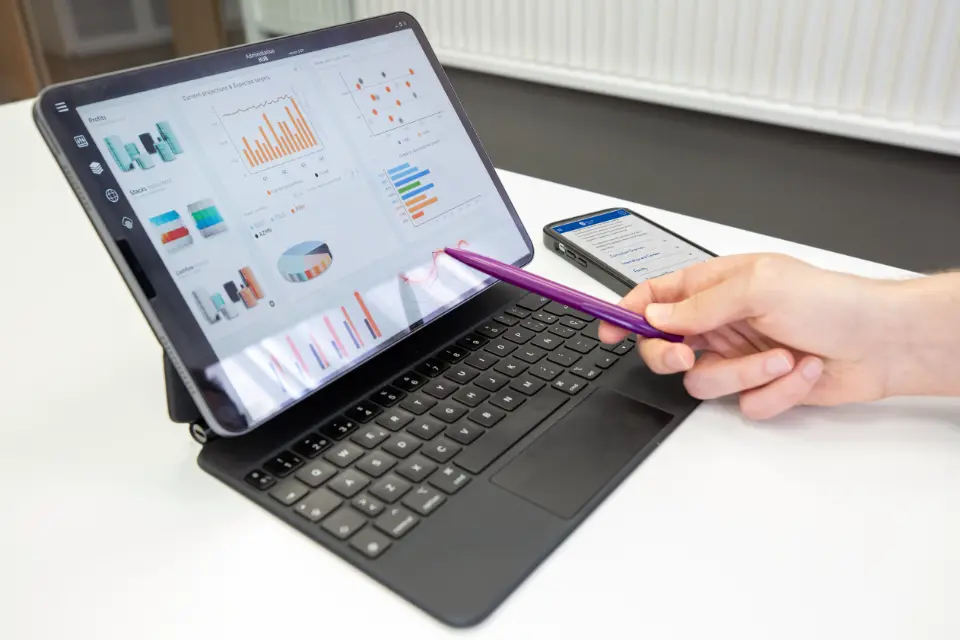 A hand pointing at a laptop screen with a pen.