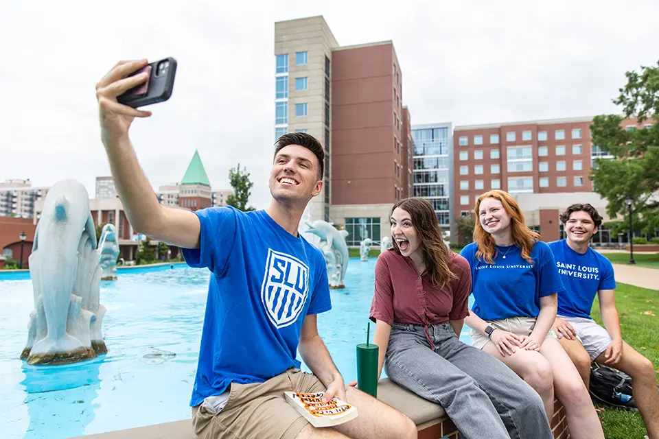 A student takes a selfie while his friends look at the camera.