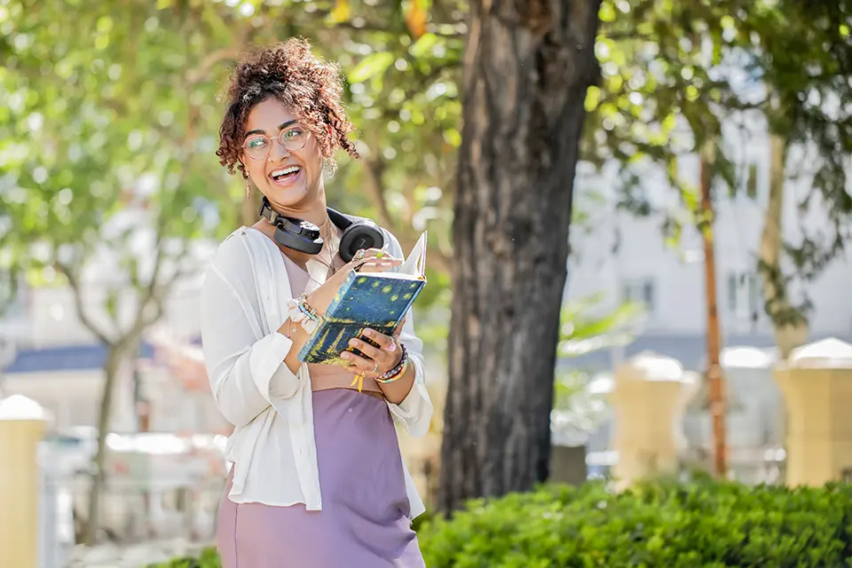 Student smiles as she holds a book in the PRH patio.