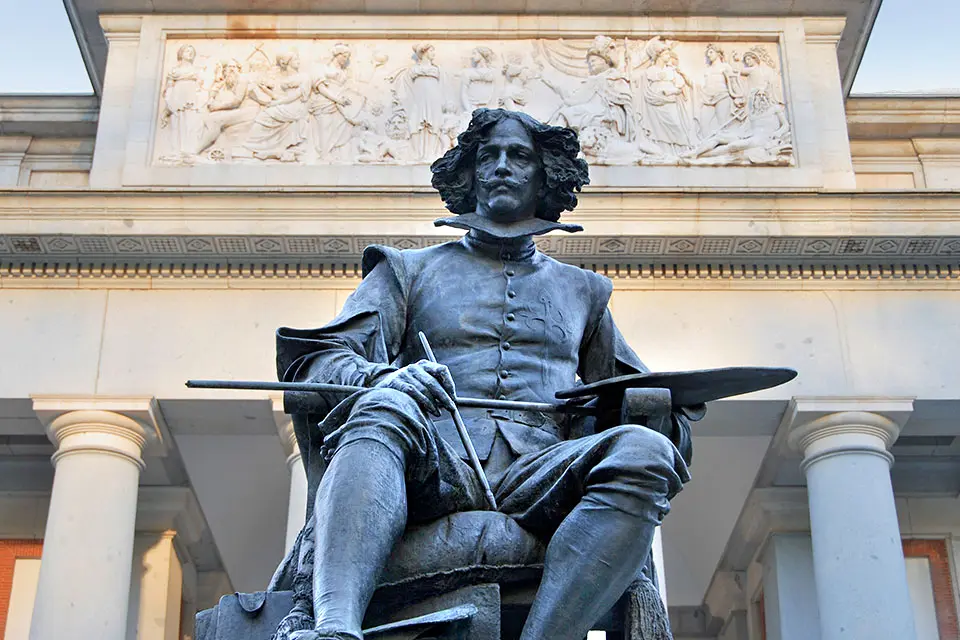 Statue of Velazquez in front of the Prado Museum. The figure is seated, holding an artist's palette and paint brushes.