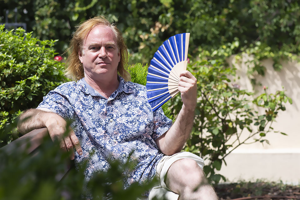Brian Goss, Ph.D. Brian Goss sits in a garden waving a fan.