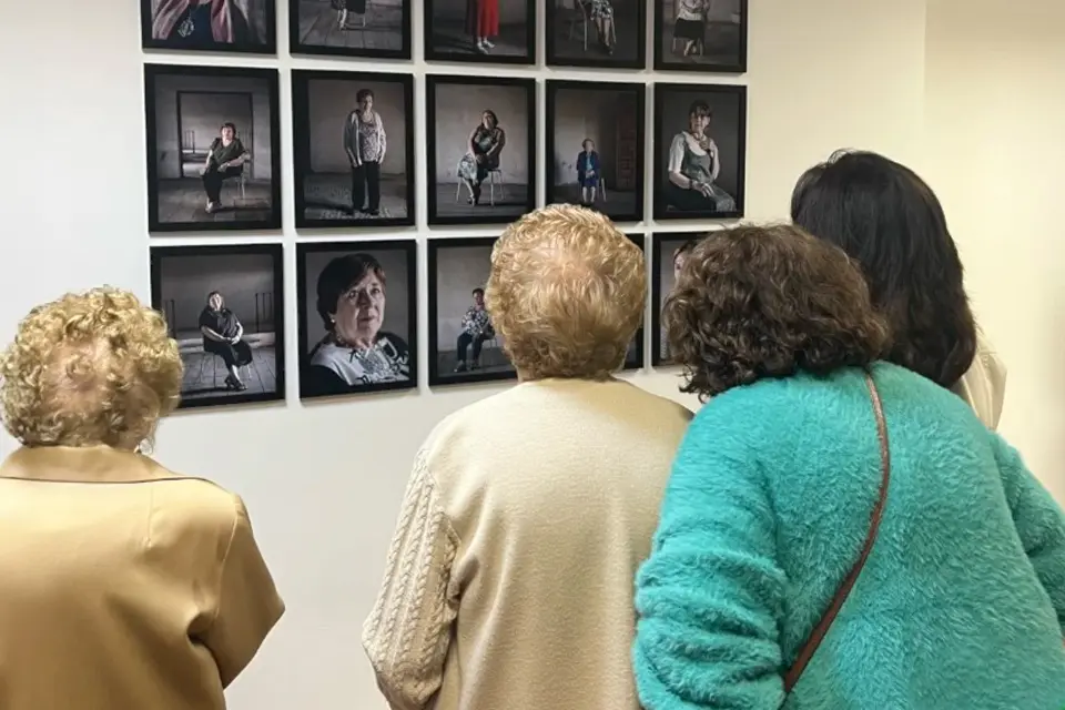 Women photographed in Fischer's "Cardos" work view photos of themselves on display at exhibit.  Women look at themselves in photographs hung on wall that are part of an art exhibit.
