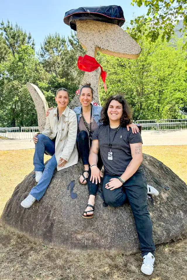 Two students and a professor pose while sitting on a rock with a sculpture made of rock behind them.