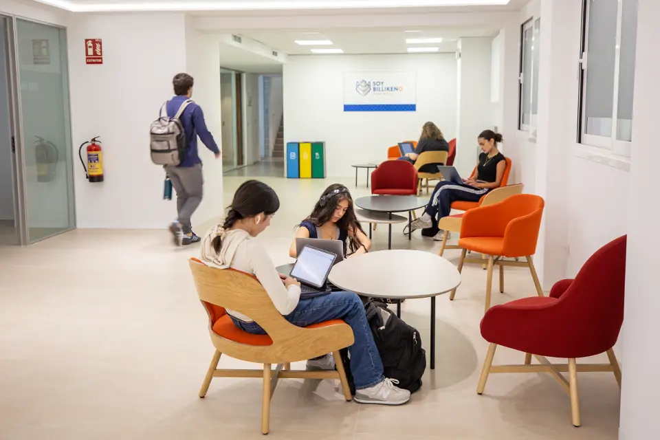 Students sitting in chairs studying on laptops in a lobby area of the building.