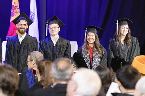 Man speaks on stage in front of podium to an auditorium full of graduating students and other attendees present.