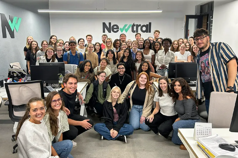 Students pose in front of agency's logo looking directly at camera. 