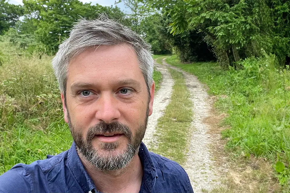 A man looking directly at the camera for a photo with a country road behind him.
