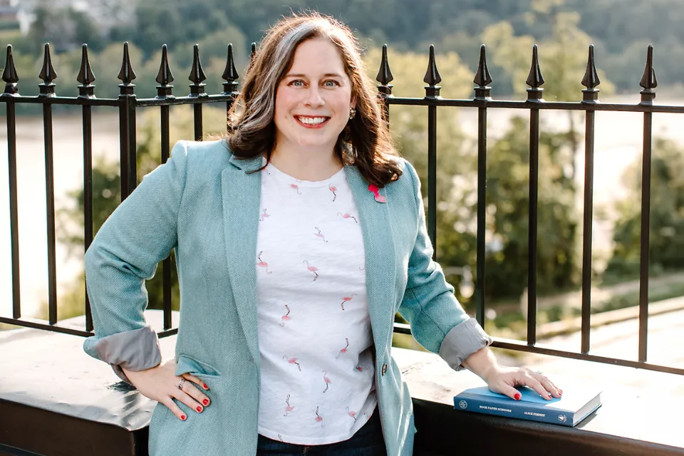 Woman in blazer smiles at camera while leaning against brick ledge of building.