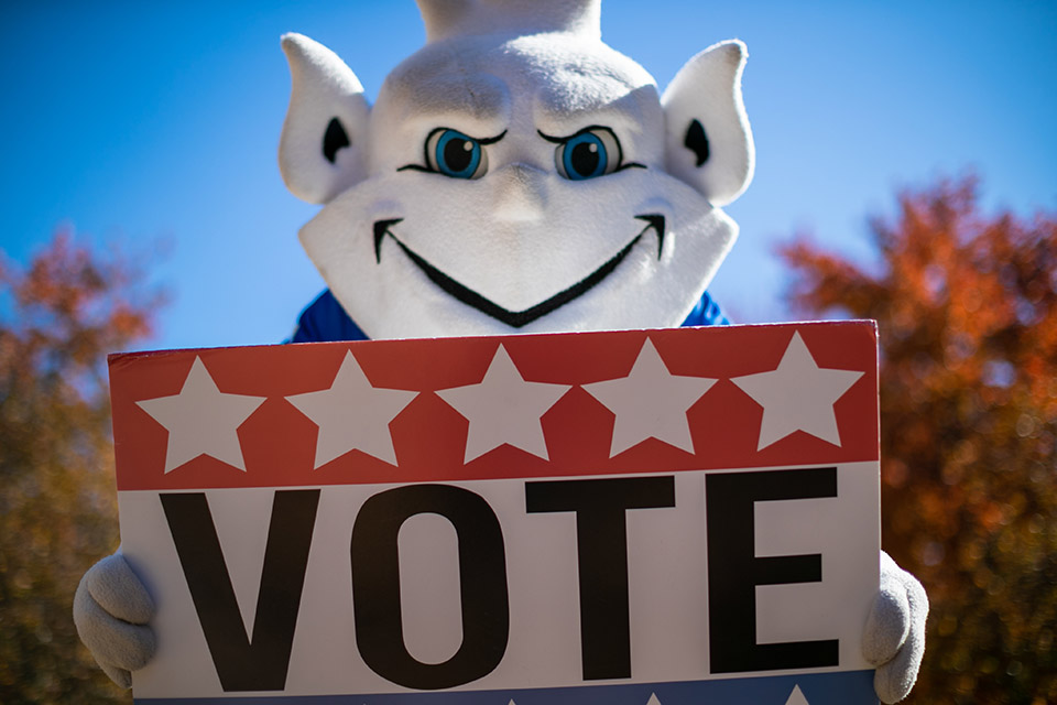 The Billiken holding a sign that says "Vote"