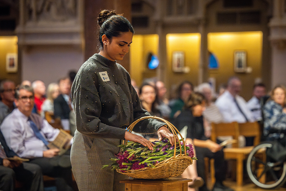 A student participates in an Interfaith Memorial Service at SLU. She places purple flowers in a basket.