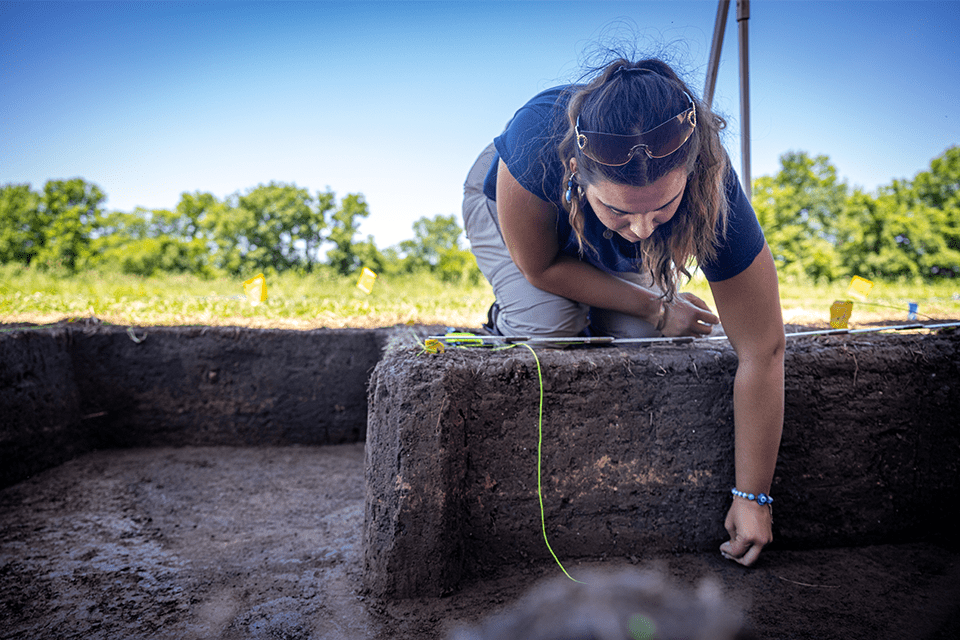 A woman leans over a dirt wall to dig out dirt from an excavation site on a sunny day at Cahokia Mounds in Collinsville, Ill.