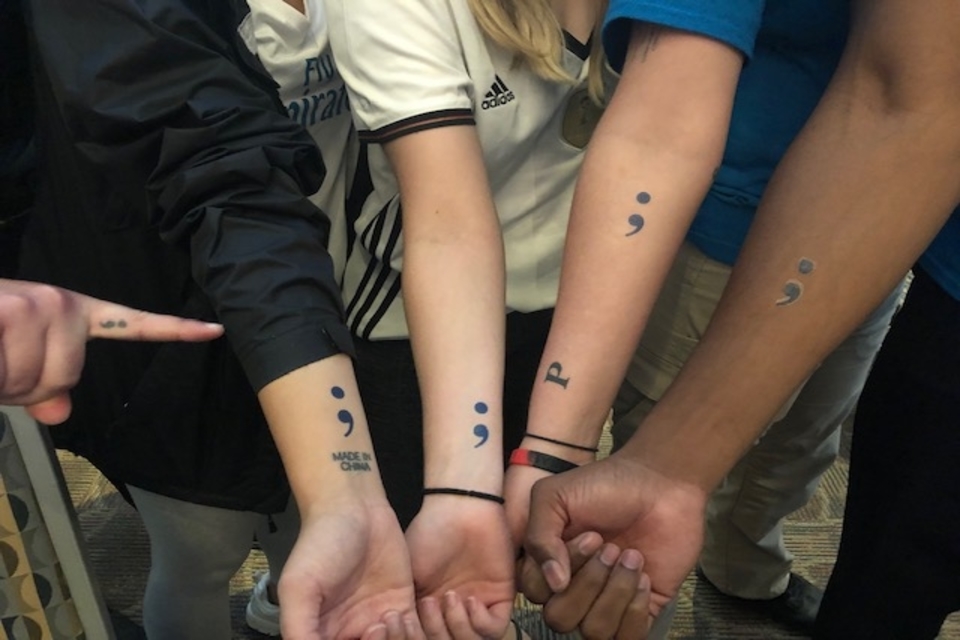 A detail of students and DPS officers showing off semi-colon temporary tattoos to mark their solidarity with those experiencing mental health and wellness issues during a 2019 Post-Secret U event.