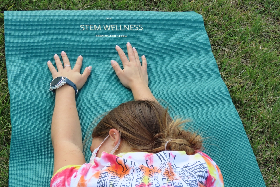 A student stretches in child's pose on a SLU STEM Wellness mat at one of the group's outdoor yoga sessions.