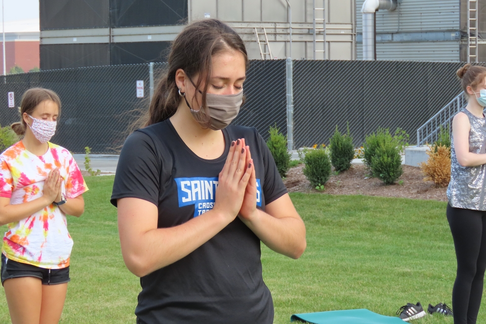 A student breathes with hands over heart at a SLU STEM Wellness outdoor yoga event.